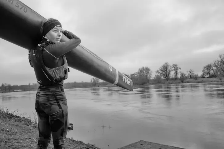 Frau trägt Boot auf der Schulter. Im Hintergrund ein Fluss.