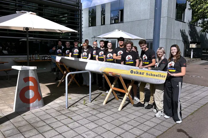15 junge Leute stehen nebeneinander. Im Vordergrund ein von ihnen konstruiertes Betonkanu.