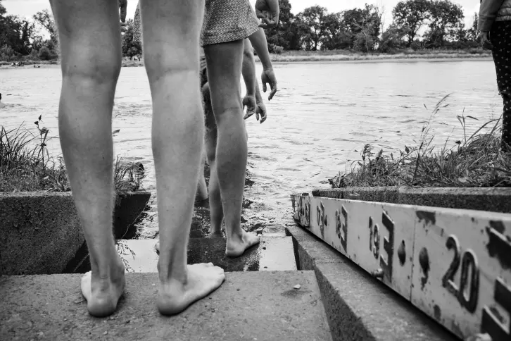 Beine von M&auml;nnern in Badehosen, die auf einer Treppe stehen und in einen Fluss steigen wollen.