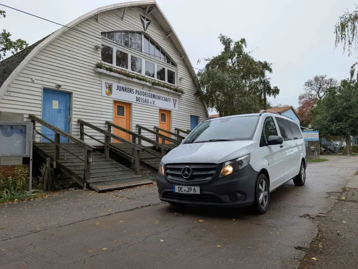 Weißer Kleinbus mit eingeschalteter Beleuchtung vrom Bootshaus.