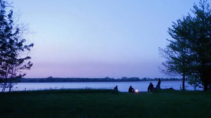 Blaue Stunde an der einem Fluss. Vier Personen sitzen an einem Lagerfeuer.