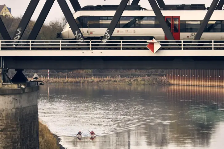 Ein Personenzug auf der Elbbrücke bei Roßlau, auf dem Fluss zewi Paddler.