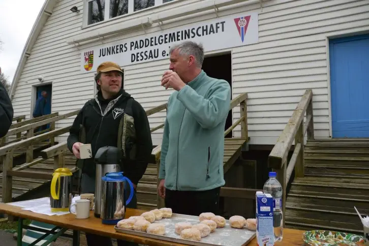 Zwei Männer stehen vor einem Bootshaus an einem Frühstücksbuffet.