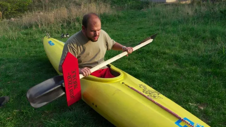 Paddler sitzt im gelben Kanu und hält einen improvisierten Wegweiser