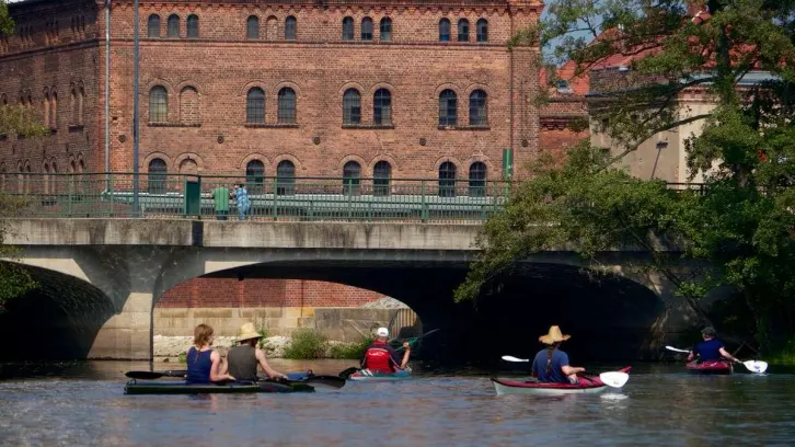 Mehrere Kanuten vor einer kleineren Autobr&uuml;cke und den historischen Mauern einer Gro&szlig;m&uuml;hle.