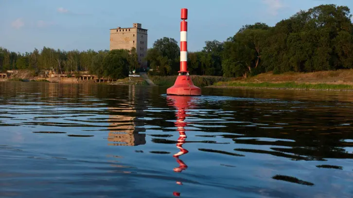 Rot-weiße Tonne in der Elbe zur Begrenzung der Fahrrinne. Im Hintergrund ein alter Speicher im Dessauer Wallwitzhafen.