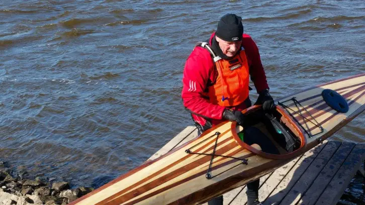 Mann mit roter Schwimmweste trägt ein Kajak.