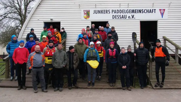 Rund 40 Menschen, viele mit Schwimmwesten, stehen vor einem Bootshaus.