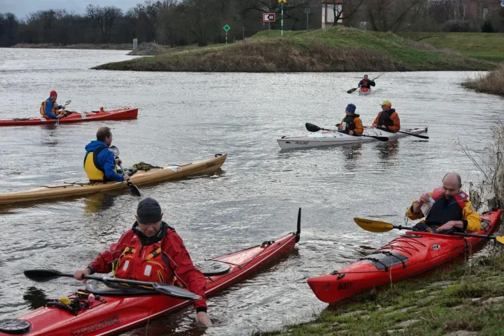 Mehrere Personen in Kajaks in der N&auml;he eine Flussufers.