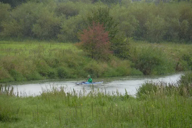 Paddler auf einem kleinen Fluss, der durch eine gr&uuml;ne Landschaft f&uuml;hrt. Es regenet etwas.