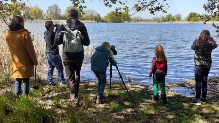 Kinder und Erwachsene am Ufer eines Sees, V&ouml;gel beobachtend