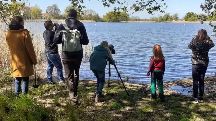 Kinder und Erwachsene am Ufer eines Sees, Vögel beobachtend