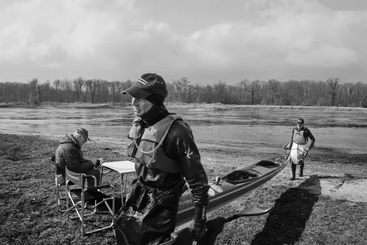 Zwei M&auml;nner tragen ein Kajak. Im Hintergrund ein Fluss.