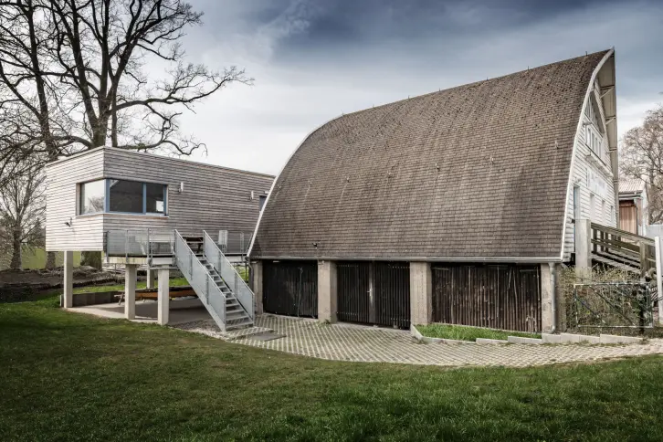 Ein historisches Bootshaus und ein moderner Erweiterungsbau. Beide mit Holzfassade.